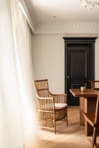 A modern living room with wooden furniture, featuring a rattan armchair and a wooden dining table with a small cup.
