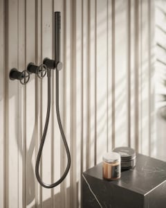 Black metallic bathroom faucet and showerhead system mounted on a white wooden panel wall.