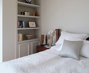 A minimalist bedroom featuring wood accents, fabric bedding, and glass vases, with a bedside table and bookshelf.