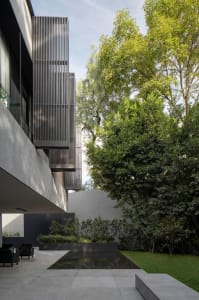 Modern house exterior with concrete walls, large glass windows, and gray metal shutters surrounding a minimalist outdoor pool