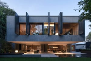 A modern residential house with concrete and glass materials, featuring large windows and a sleek, contemporary design.