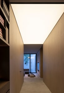 A modern living room with wooden walls and floor, featuring a minimalist sofa and a large window.