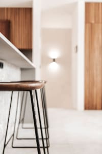 A modern minimalist kitchen with wooden accents, concrete countertops, and black metal stools.