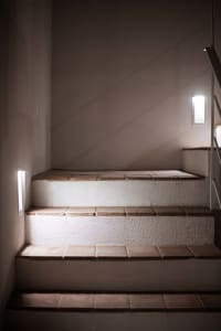 Modern staircase with tile steps and walls, illuminated by wall sconces.