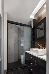 Modern bathroom interior with marble and black tile walls and floor, featuring a sink with a white countertop and black cabin