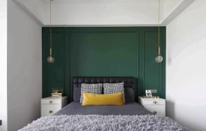 A modern bedroom featuring a green accent wall, black and white checkered pillows, and a grey bedspread.