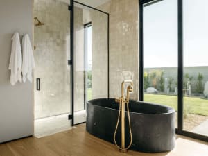 Modern bathroom with a freestanding black marble tub, glass shower enclosure, and white towels hanging on the wall.