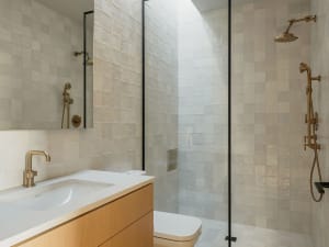 A modern bathroom with white and beige square tiles, a white sink, and a walk-in shower with glass doors.