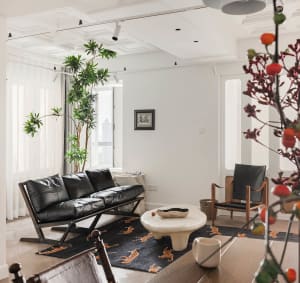 Modern minimalist living room with black leather sofa, white marble table, and wooden furniture, set against a white wall and