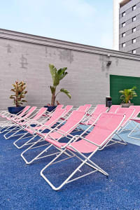 A row of pink foldable outdoor chairs arranged neatly in a poolside area with plants and a blue textured surface.