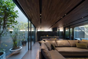 Modern living room with a wooden ceiling and floor, featuring a large sectional sofa and a connected dining area.