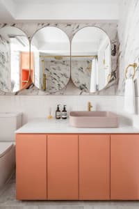 Modern bathroom with marble walls, concrete flooring, pink cabinets, and pink sink.