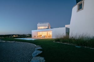 A modern house with white painted exterior and concrete terraces viewed at night with lights on showing interior space.