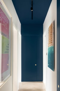 A hallway with navy blue walls and white doors, featuring framed colorful artworks on the walls.