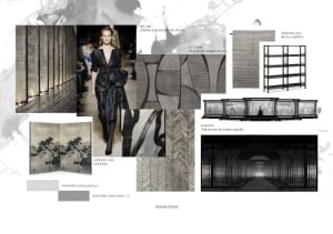 Model wearing a black outfit at a runway show with patterns and textures displayed in the background.