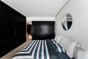 A modern minimalist bedroom with a striped blue and white bedspread, black cabinets, and a round mirror on the wall.