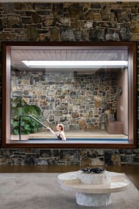 A modern living space featuring stone walls and a glass enclosure with a woman in a pool.