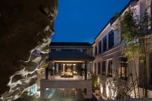 An outdoor space at night with concrete walls, a glass pavilion, and plants.