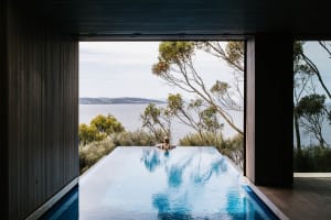Person in a modern house with a glass infinity pool overlooking a teal-colored skyline.
