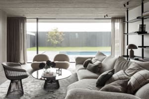 Modern living room with fabric furniture, minimal decor, and large glass windows overlooking a pool.
