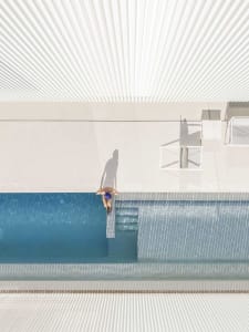 A modern white plaster pool area with a person walking towards the edge.