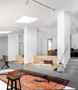 A minimalist living room features wooden benches and a large rug in a modern space.