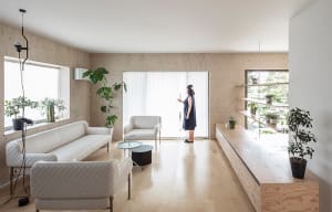 A minimalist living room featuring white sofas, a coffee table, and wooden paneling with plants.