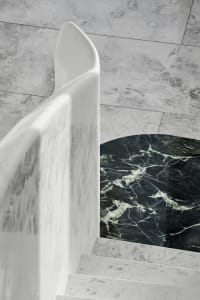 Modern marble staircase with curved handrail and textured floor.