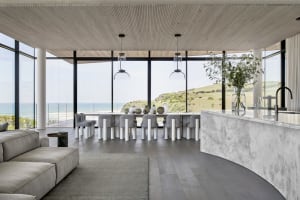 Modern residential interior with large glass windows overlooking a scenic coastal landscape, featuring a concrete and glass d