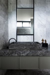 A modern marble bathroom with a sleek, dark marble countertop and sink, positioned under a rectangular mirror.