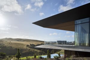 A modern house with a glass exterior overlooking a hilly landscape.