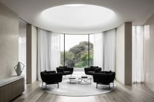 A modern living room with black armchairs, a round coffee table, and a large round rug with large windows and sheer curtains 