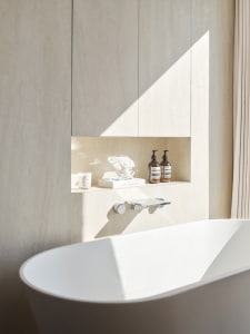 A minimalist bathroom featuring a white bathtub with a concrete wall and shelves.