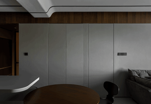 Modern minimalist living room with concrete walls, wooden furniture, and a black chair.