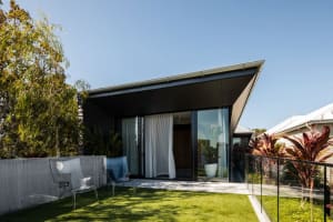 A modern house exterior featuring glass walls, concrete patio, and surrounding greenery.