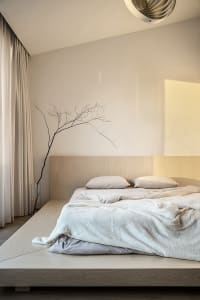 Minimalist bedroom featuring a platform bed with wood frame, white bedding, and a glass vase with a branch as decor.