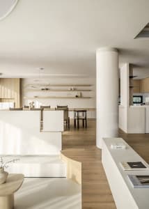 A modern minimalist kitchen and living space featuring white walls, wooden furniture, and open shelving.