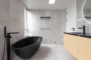 A modern bathroom featuring a black freestanding bathtub, concrete walls, and wooden vanity.