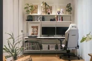 A modern and industrial home office featuring a grey gaming chair, multiple monitors, and decorative elements on shelves.