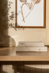 Modern shelving unit with beige canvas and wire绑带装饰，背景为浅色墙面和植物阴影。