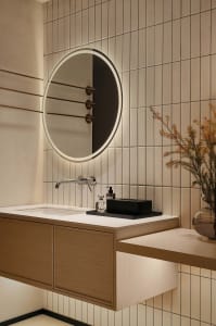 Modern bathroom design featuring a circular mirror and a sink with ceramic tiles on the walls.