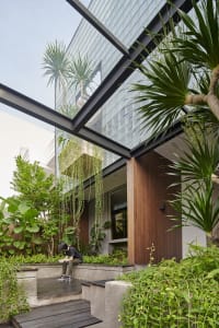 A modern housefront featuring large glass panels, wooden accents, and lush greenery.