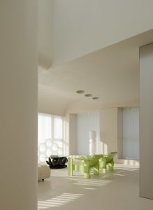 A minimalist living room with green chairs, white furniture, and a glass table.
