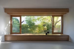 A minimalist residential space featuring a large window seat with wooden cabinets and a view of lush greenery outside.