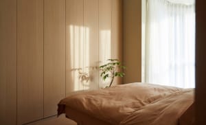 A minimalist bedroom with a textured wooden bed and window allowing soft light to filter in.