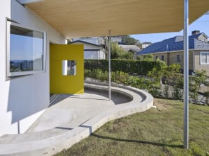 Modern backyard with concrete patio, yellow geometric wall, and greenery.