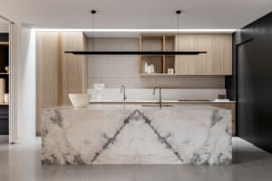 Modern industrial kitchen featuring a marble island counter with sink and faucet, wood cabinetry, and a black pendant light f