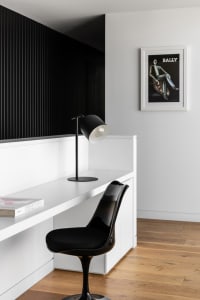 A minimalist home office features a white desk with a black lamp and chair, set against a black and white striped wall and wo