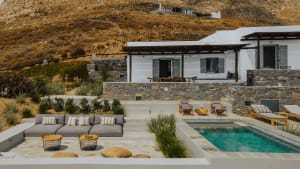 Modern residential backyard featuring a concrete patio, sofa, chairs, pool, and stone walls.