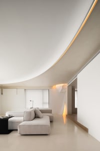 Modern minimalist living room with concrete walls and floor, featuring a white sectional sofa and a sleek, low-profile coffee